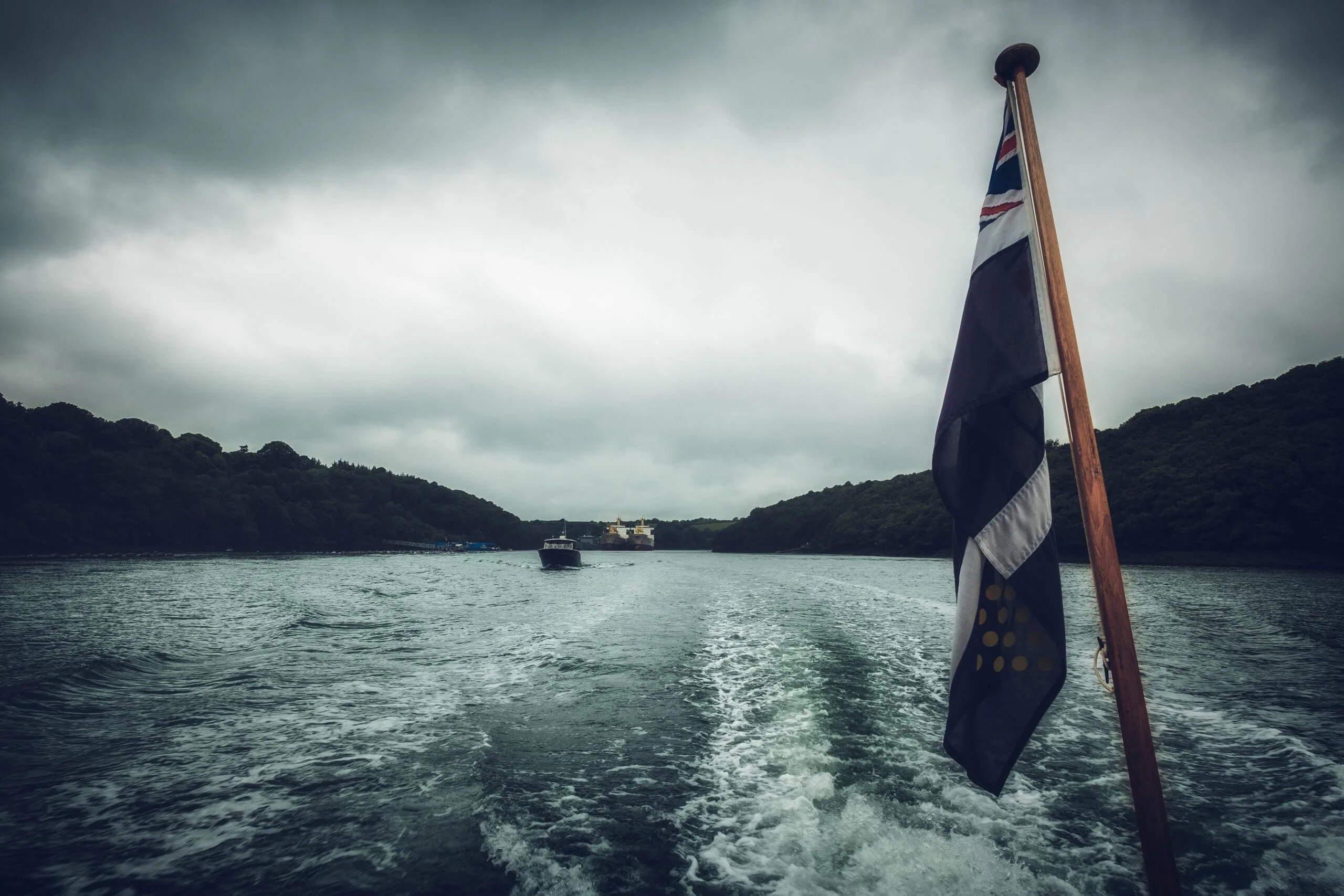 The Cornish flag in the foreground with the wake of the boat in the background